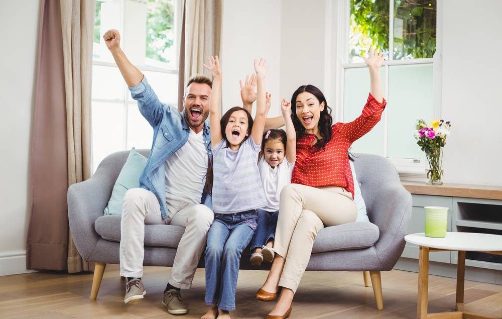 família com pai, mãe e duas filhas comemorando no sofá da sala