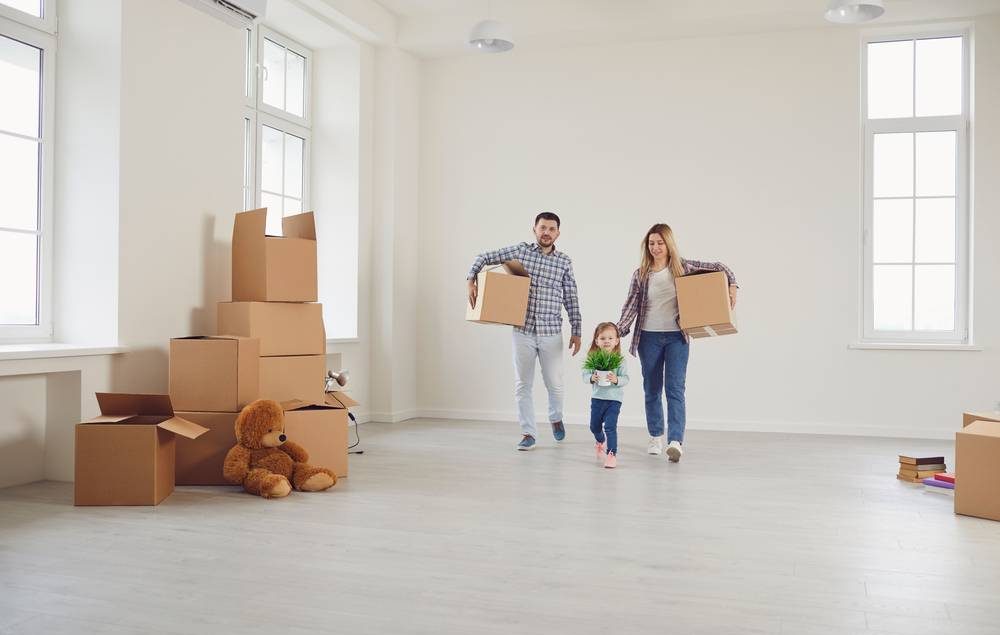 Família com pai, mãe e filha, brancos, em um apartamento vazio com caixas espalhadas