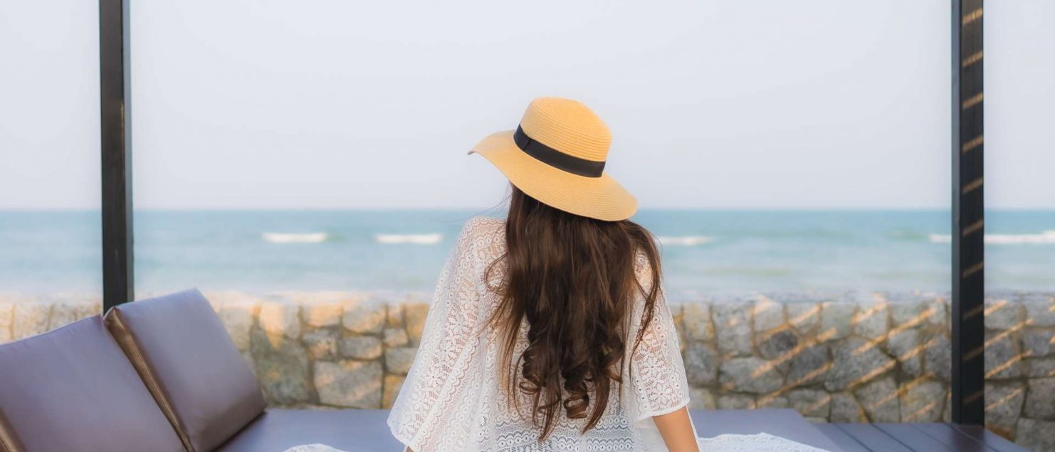 mulher sentada de costas em cadeira de sol acolchoada em frente a praia