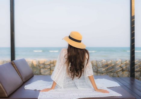 mulher sentada de costas em cadeira de sol acolchoada em frente a praia