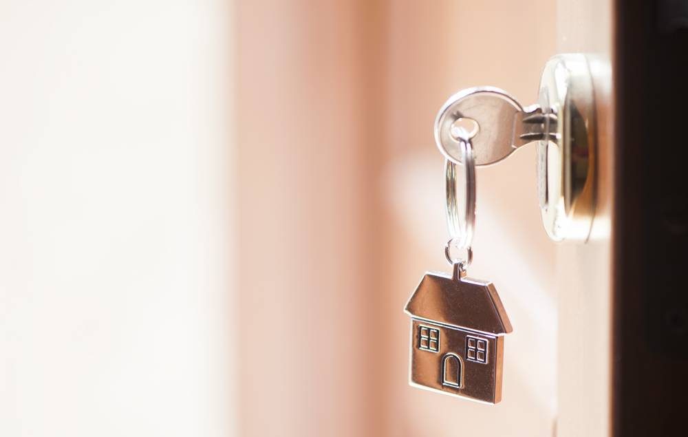 imagem focada em um chaveiro de aço com uma casa, em uma chave na porta