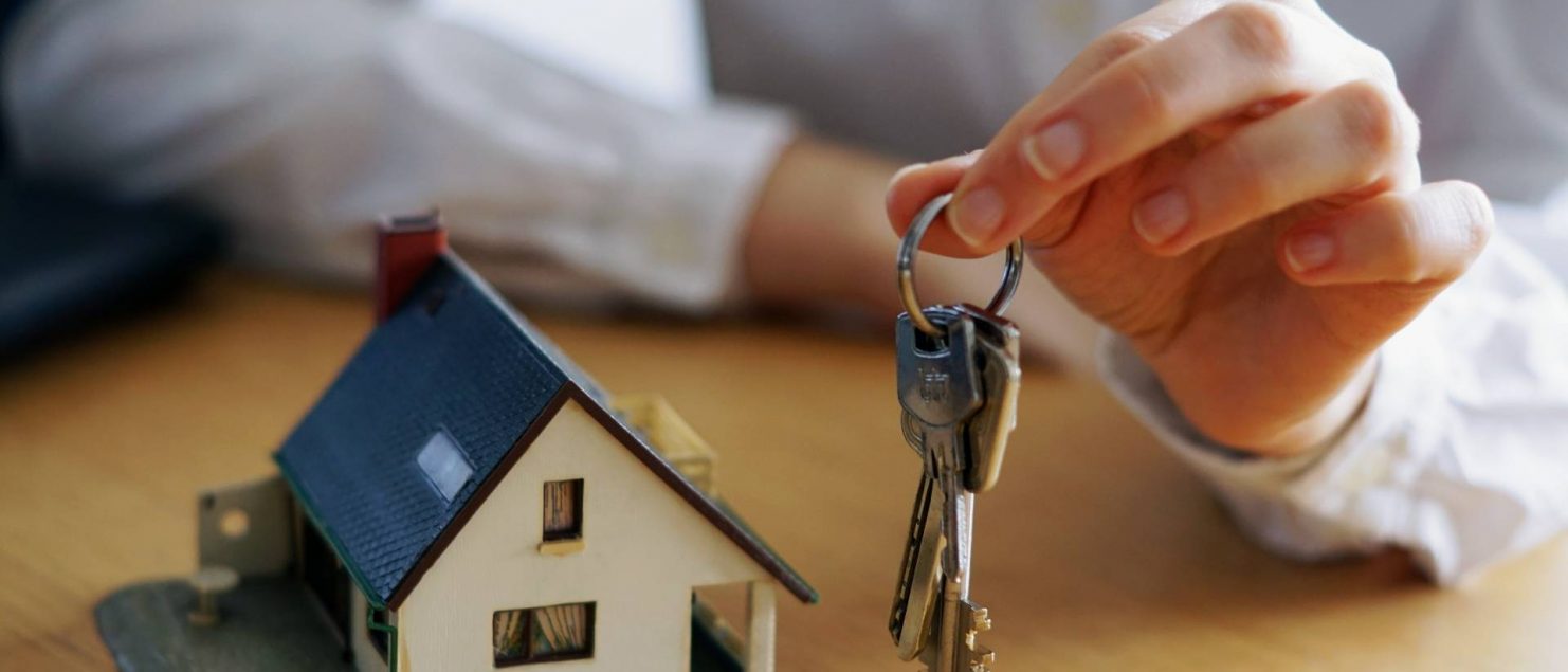 maquete de casa branca com telhado azul e mão masculina segurando chave