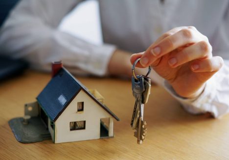 maquete de casa branca com telhado azul e mão masculina segurando chave