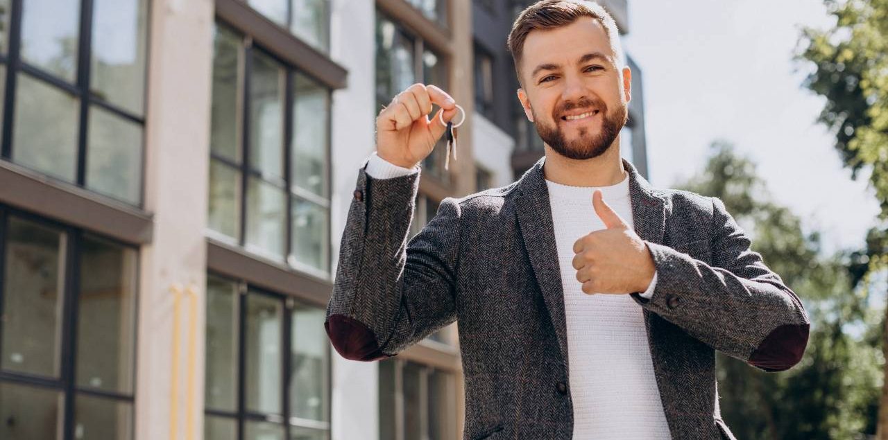 homem branco com chaves na mão em frente a predio