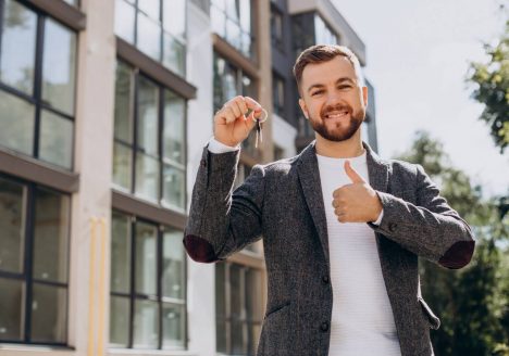 homem branco com chaves na mão em frente a predio