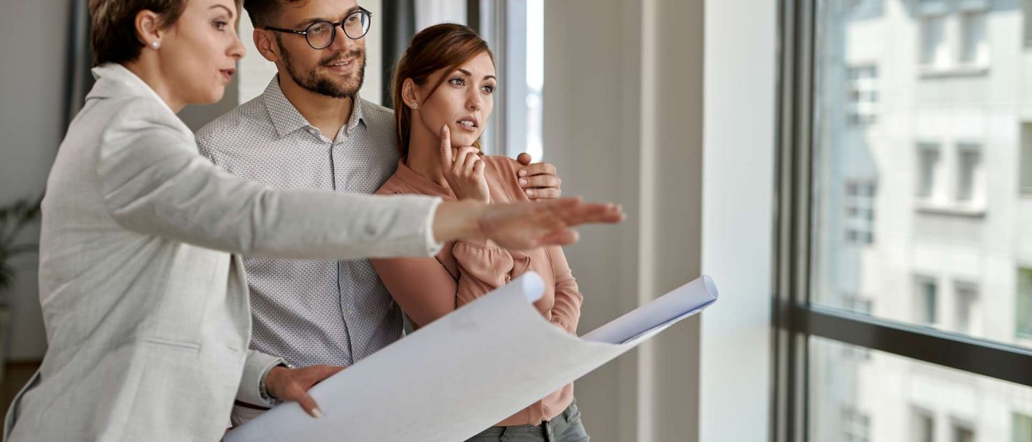 jovem-casal-examinando-plantas-com-agente-imobiliario-ao-comprar-uma-nova-casa