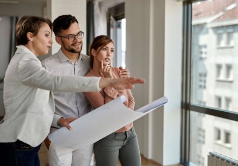 jovem-casal-examinando-plantas-com-agente-imobiliario-ao-comprar-uma-nova-casa