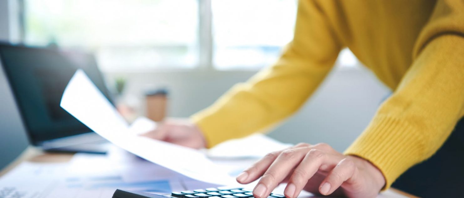 mãos fazendo contas com uma calculadora e papel na mão